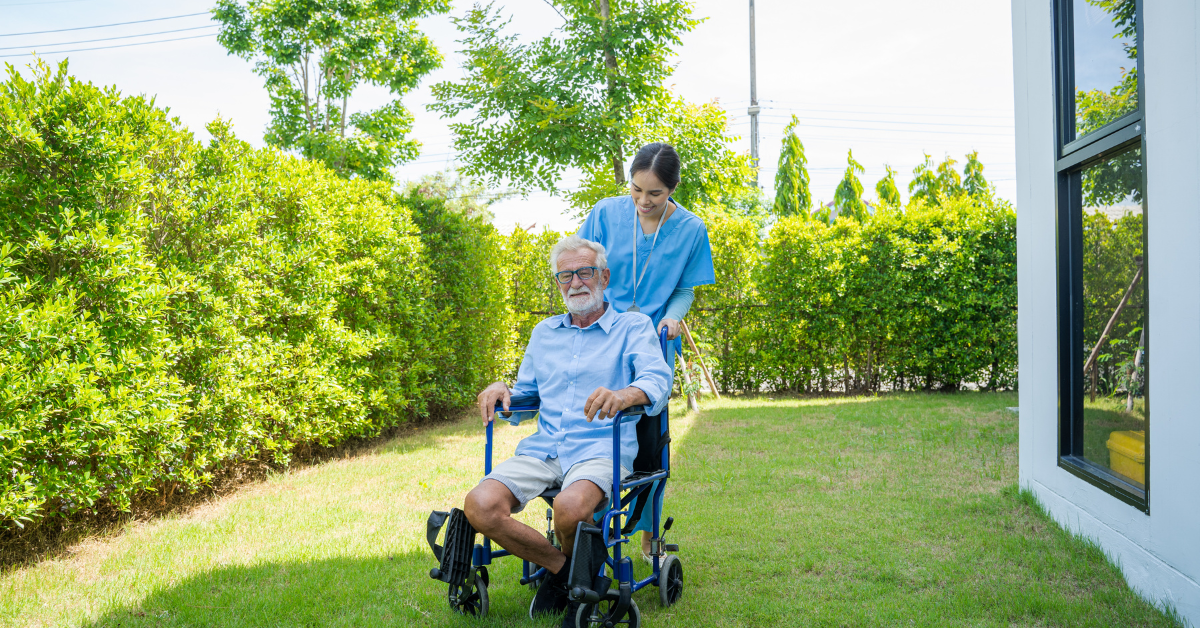 specialist disability accommodation - A nurse is helping an old man with his wheelchair in a green-ish place