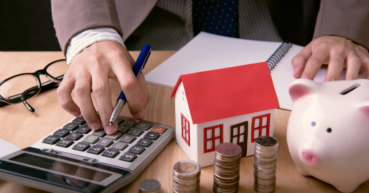 NDIS Property Loan - A person is calculating loan on a calculator and there is a dummy house and coins and piggy bank on the table
